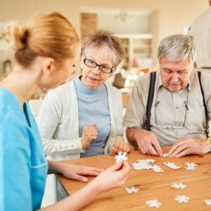 Elderly couple assembling a puzzle with caregiver assistance.