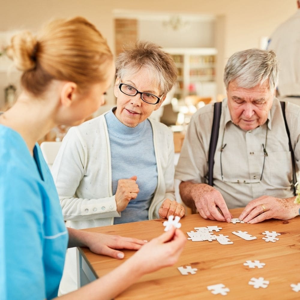 Elderly couple assembling a puzzle with caregiver assistance.