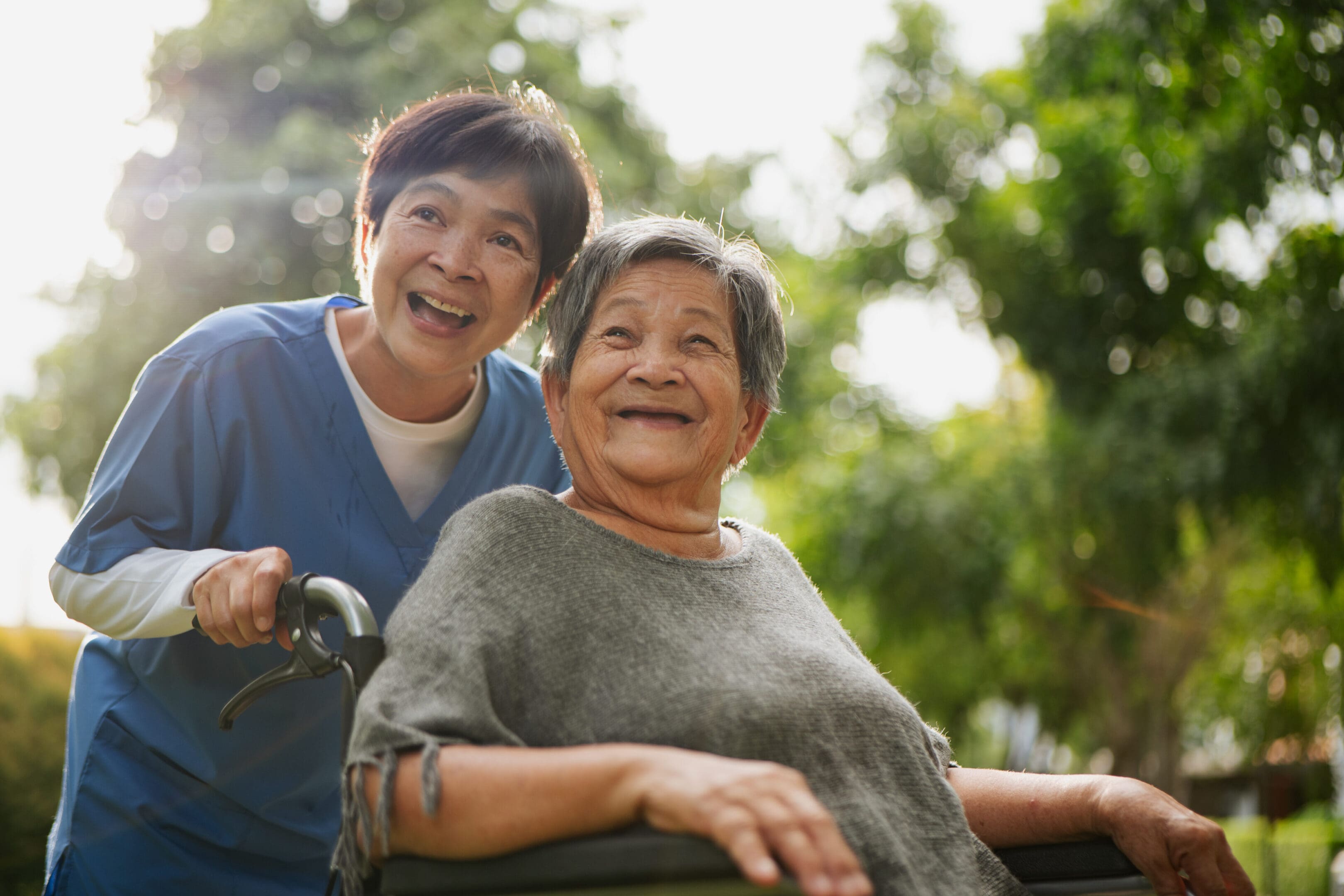 Asian elderly woman in a wheelchair relaxing with her caregiver in a peaceful public park.