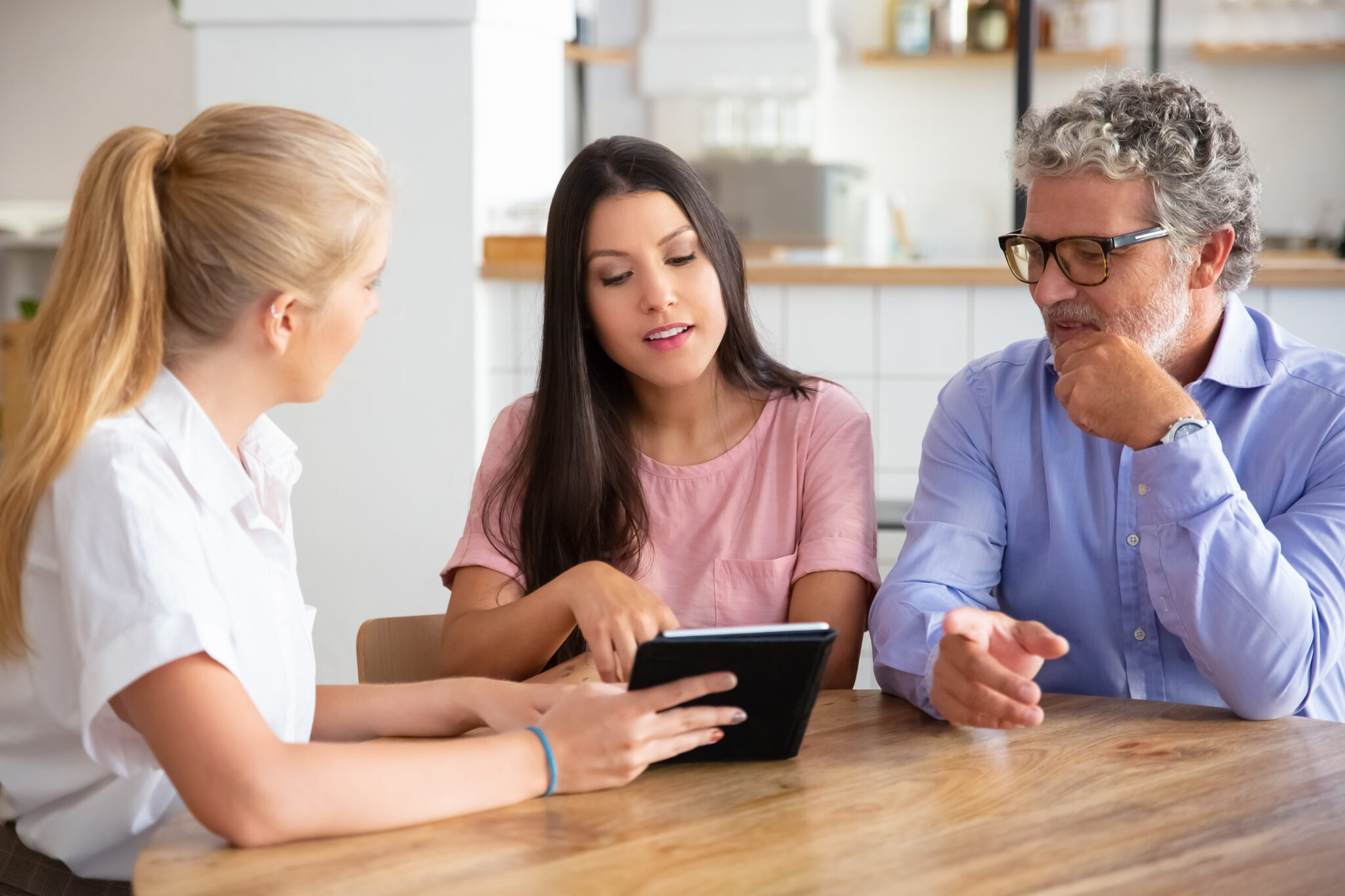 Female consultant or manager meeting with couple of young and mature customers, presenting content on tablet. Man and woman looking and pointing at screen. Consulting or technology concept