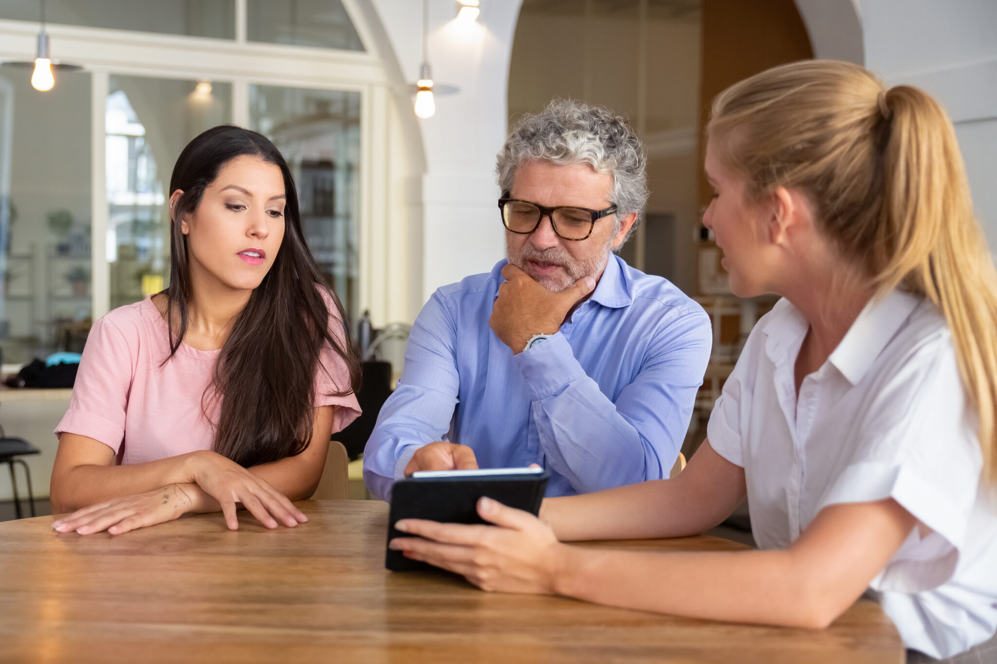 Pensive serious young woman and mature man meeting with female professional, watching and discussing content on tablet. Consulting or cooperation concept