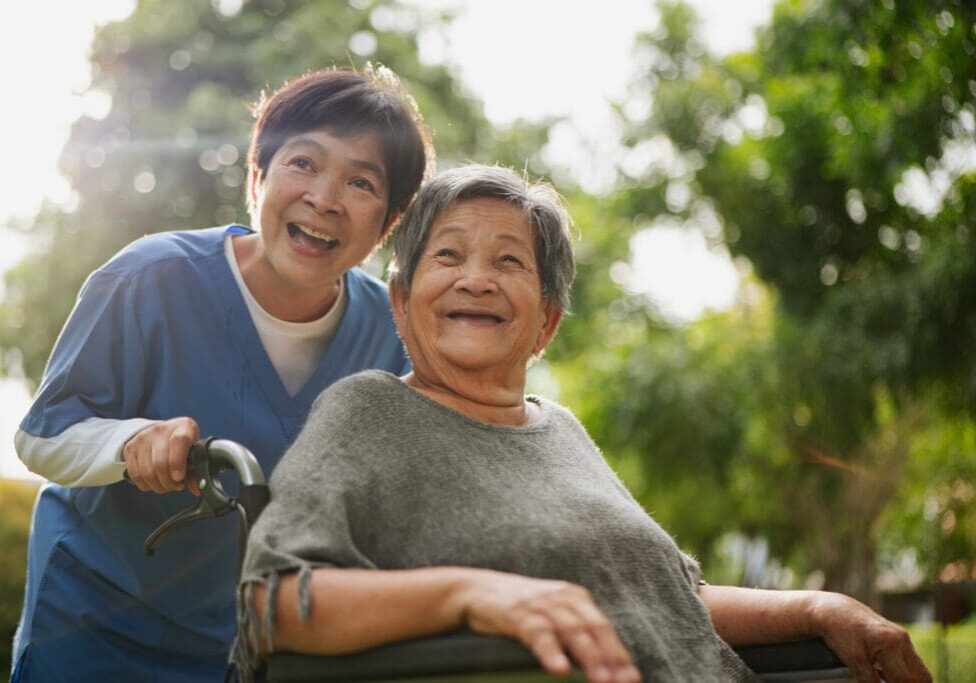 Asian elderly woman in a wheelchair relaxing with her caregiver in a peaceful public park.